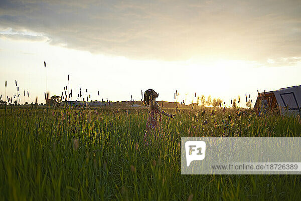 Young girl running in a field of high grass whilst out camping