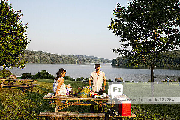 A young couple enjoy a picnic at a state park near a lake.