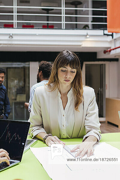 Businesswoman sitting at desk in office measuring plan