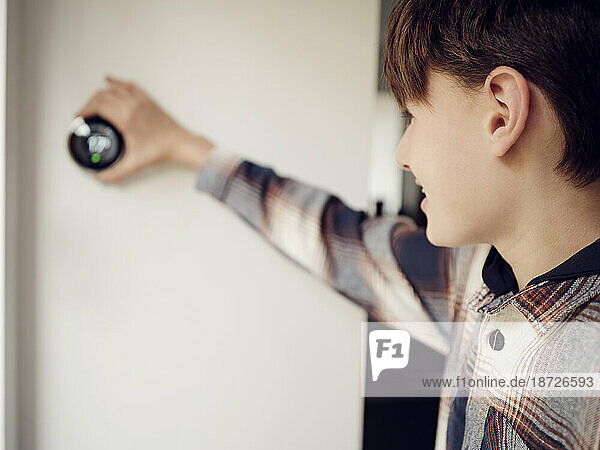 Boy adjusting smart thermostat control on the wall at home