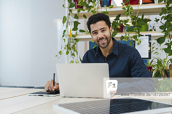 Portrait of smiling businessman with digital tablet  laptop and solar panel on desk