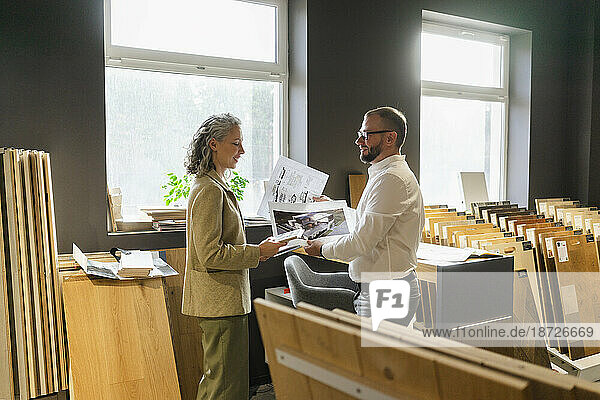 Two colleagues holding printout of a house and blueprint in architect's office