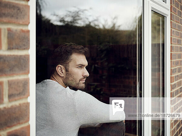 Nachdenklicher Mann schaut zu Hause aus dem Fenster