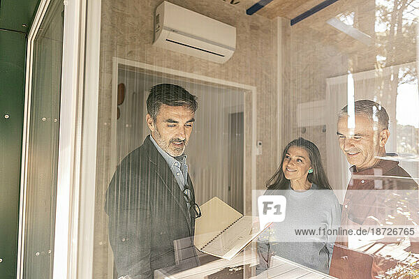 Real estate agent discussing purchase contract with new home owners standing at window