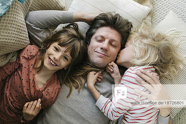 Happy father lying with daughters on pillows at home