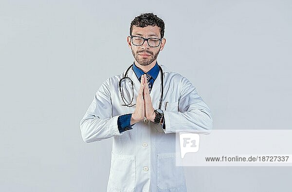 Arzt betet mit den Händen zusammen auf isoliertem Hintergrund. Junger Arzt betet mit den Händen zusammen isoliert