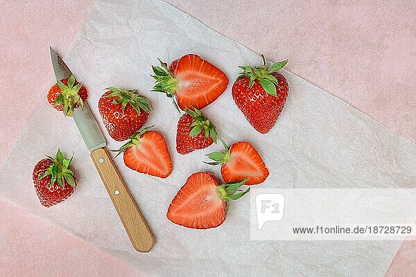 Ganze und halbierte Erdbeeren (Fragaria) mit Küchenmesser