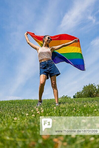Caucasian brunette Frau mit einem Regenbogen lgbt Flagge auf dem Gras und blauen Himmel Hintergrund  winken die Flagge
