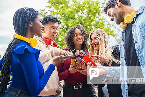 Gruppe junger lächelnder multiethnischer Freunde  die auf dem Campus in der Stadt Handys benutzen. Technologie süchtig Millennial Gemeinschaft Konzept. Social Media Kommunikation Generation Z