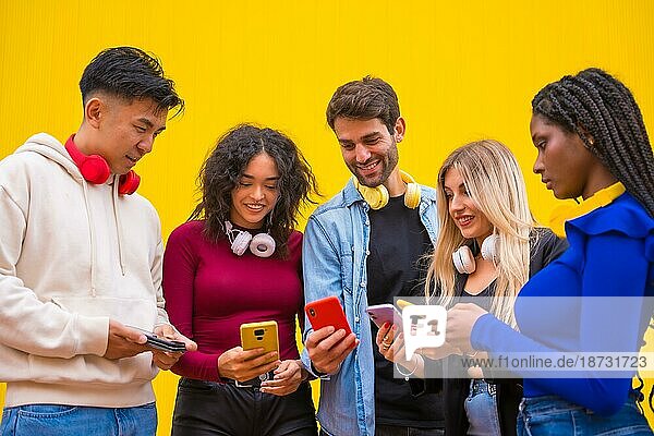 Niedriger Blickwinkel auf eine Gruppe junger multiethnischer Teenager-Freunde  die Mobiltelefone auf einem gelben Hintergrund benutzen. Technologie süchtig Millennial Gemeinschaft Konzept. Social Media Kommunikation Generation Z