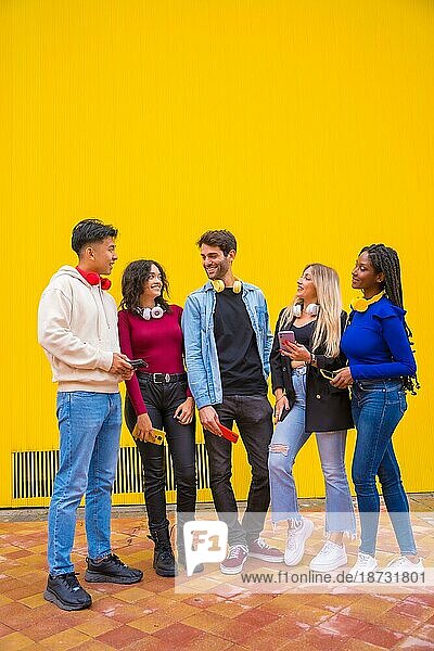 Porträt einer Gruppe lächelnder junger multiethnischer Freunde im Teenageralter  die Mobiltelefone auf einem gelben Hintergrund benutzen. Technologie süchtig Millennial Gemeinschaft Konzept. Social Media Kommunikation Generation Z