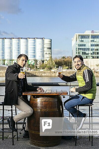 Zwei Freunde trinken und stoßen mit Bier in einer Brauerei an. Sie schauen beide in die Kamera