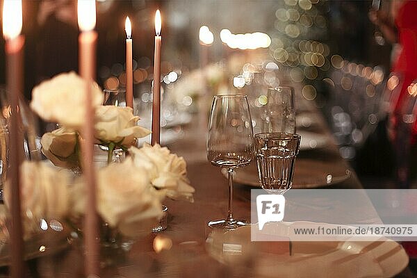 Brennende Kerzen und frische Blumen auf dem Banketttisch neben Tellern und Glaspokalen am Abend