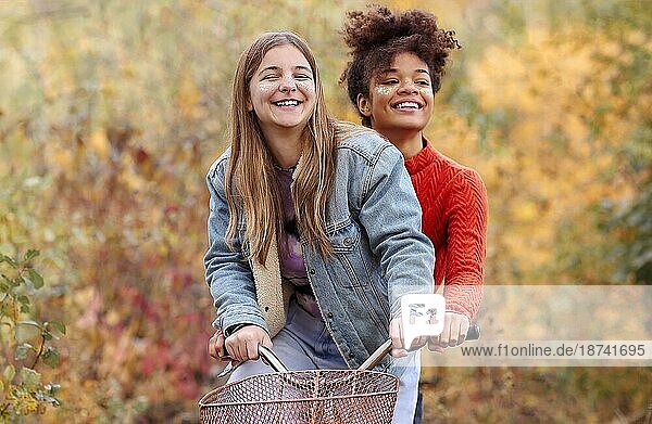 Zwei junge glückliche verschiedene weibliche beste Freunde fahren Fahrrad zusammen im Herbst Wald  aktive positive multirassische weibliche Freunde lächelnd in die Kamera  während stehend mit Stadt Fahrrad im Herbst Natur