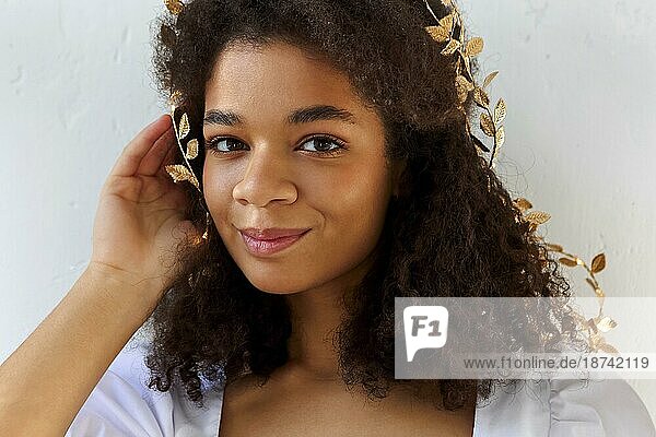 Close up Porträt der niedlichen afrikanisch amerikanischen Frau mit lockigem Haar in Blattgold Stirnband suchen flirty in die Kamera vor weißem Hintergrund  schöne Frau mit Melanin reichen Hautton. Natürliche afrikanische Schönheit