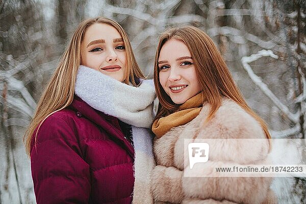 Zwei glückliche Freundinnen genießen das verschneite Wetter im Freien  Frauen beste Freundinnen in Winterkleidung Daunenjacken lachen und haben Spaß beim Spaziergang auf Stadtstraße im Winter während der Weihnachtsferien