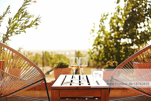 Zwei Gläser Weißwein auf rustikalen Holztisch und Blumentöpfe auf der Terrasse außerhalb mit Weinberg Hügel Landschaft am sonnigen Tag Morgen im Sommer Zeit