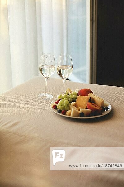 Graues Sofa mit zwei Gläsern Weißwein und frischem Obst auf dem Teller drinnen im Sommer sonnigen Abend