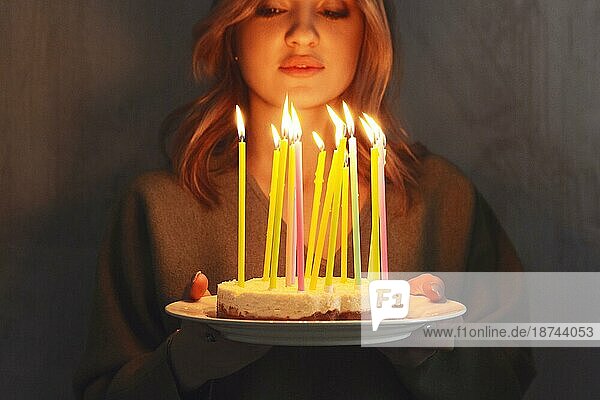 Junge lächelnde Frau hält selbstgebackenen Geburtstagskuchen mit brennenden Kerzen  während sie drinnen steht  Seitenansicht. Weibliche bringen Bday Kuchen. Geburtstag Traditionen und Feier Konzept