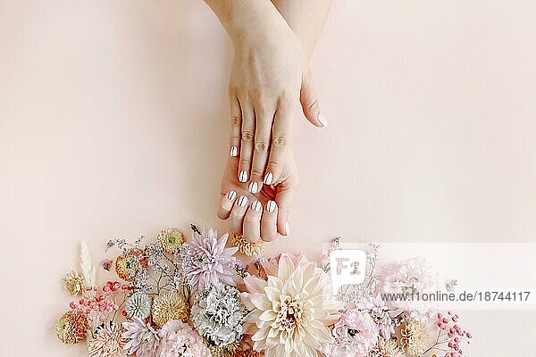 Draufsicht auf Ernte unerkennbar weiblich mit blühenden Blumen demonstrieren stilvolle saubere Maniküre auf rosa Hintergrund