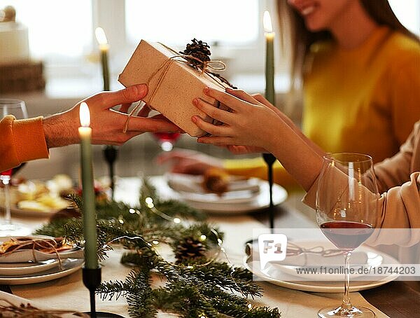 Glückliche Person  die einem Freund ein eingepacktes Geschenk gibt  während sie am Tisch sitzt und gemeinsam Weihnachten feiert