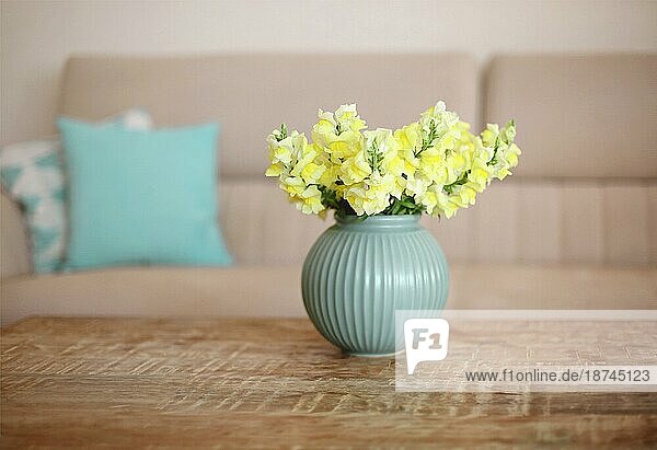 Leere Wohnung mit minimalistischen modernen Stil Interieur  hölzernen Couchtisch mit Blumenstrauß von gelben Blumen in blaün Vase in gemütlichen Wohnzimmer mit Sofa auf unscharfen Hintergrund  selektiven Fokus