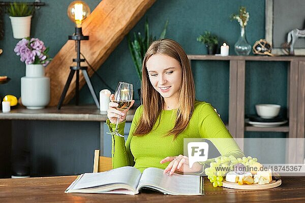 Junge Frau liest eine interessante Zeitschrift an einem Holztisch mit Obst und Wein an einem Wochenende zu Hause