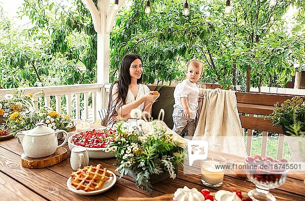 Zufriedene Frau mit süßem kleinen Kind  das sich in einem hölzernen Pavillon im Garten entspannt  während es ein Wochenende auf dem Lande verbringt