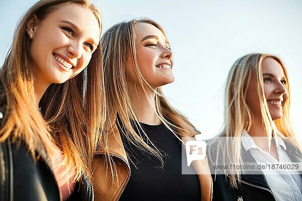 Glückliche junge Frauen  die an einem sonnigen Wochenendtag auf einer Straße in der Stadt auf dem Bürgersteig gehen und lächeln