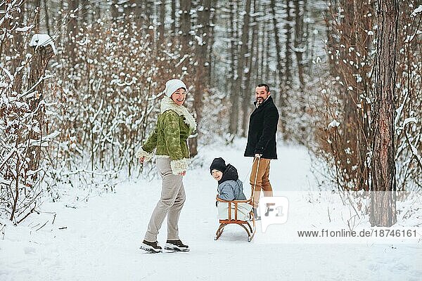 Fröhliche Eltern  die hinter einem fröhlichen Jungen gehen  der seine Zeit im verschneiten Wald an einem Wintertag verbringt