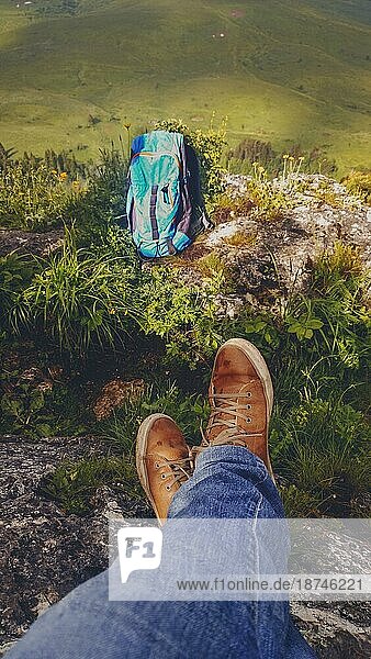 Wanderrucksack und Beine in Sportschuhen einer jungen Frau  die sich bei einer Bergwanderung im Tal ausruht  aktiver gesunder Lebensstil im Freien Erholung