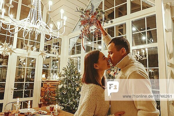 Mitternachtskuss. Junge glückliche Familie Paar in der Liebe küssen und umarmen während Silvesterfeier in gemütlichen festlich geschmückten Raum mit Weihnachtsbaum und festlichen Esstisch