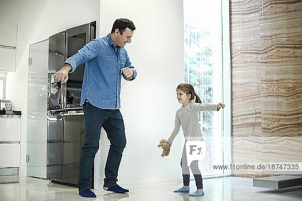 Glücklicher Vater und Tochter tanzen im Korridor am Fenster zu Hause. Familienleben Konzept