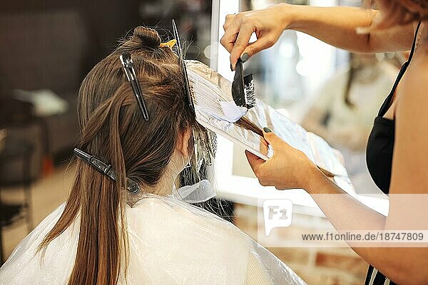 Unbekannte Friseurin schmiert Farbstoff auf das Haar einer Frau  die in einem Schönheitssalon arbeitet
