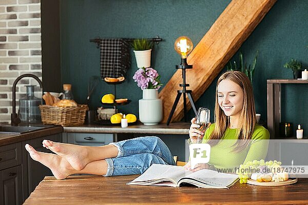 Junge Frau liest eine interessante Zeitschrift an einem Holztisch mit Obst und Wein an einem Wochenende zu Hause