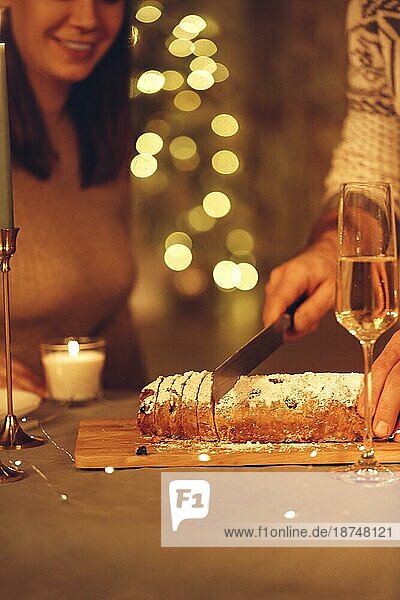 Selektive Fokus der weiblichen Schneiden leckeren frisch gebackenen hausgemachten Kuchen xms mit Messer  feiern Heiligabend oder Silvester mit Freunden oder Familie zu Hause mit LEDlichter geschmückt  defokussiert. Stollen