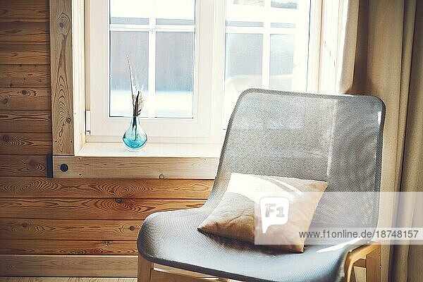 Innenraum des gemütlichen modernen Haus mit ethnischen Boho Dekoration. Sessel mit Kissen auf Holzboden  Vorhänge auf großes Fenster im rustikalen Wohnzimmer in sonnigen Tag  niemand  flach legen  freien Raum