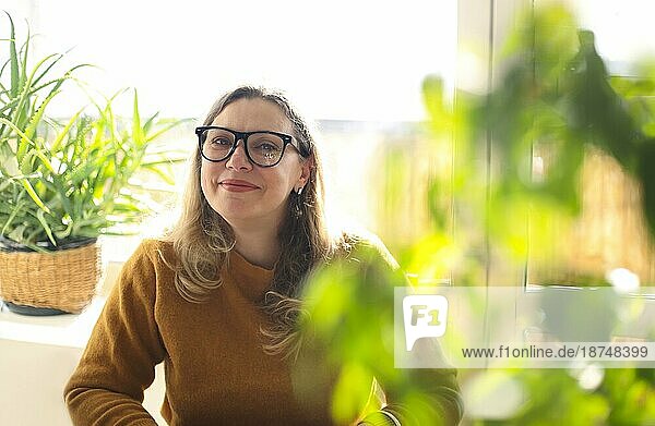 Porträt einer lächelnden Frau mittleren Alters mit Brille  die in einem Raum mit grünen Zimmerpflanzen sitzt  selektiver Fokus. Positive glückliche 40er Jahre Lehrerin mit Brille im Grünen  arbeitet in der Schule