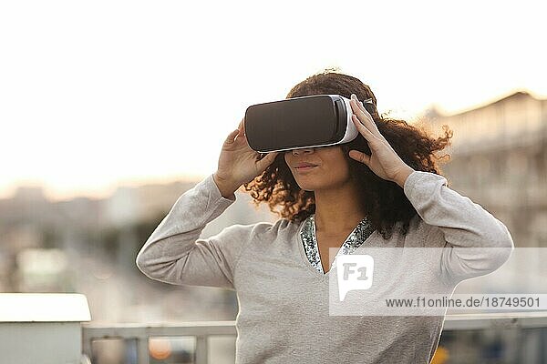 Technologie der Zukunft. Junge  moderne  gemischtrassige Frau mit VR Brille  die die virtuelle Realität im Freien mit einer Stadtlandschaft im Hintergrund erkundet  eine Frau  die versucht  mit dem Cyberspace zu interagieren