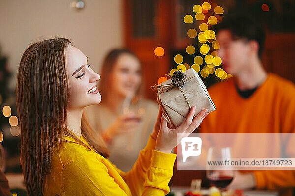 Junge Person  die einem Freund ein eingepacktes Geschenk gibt  während sie am Tisch sitzt und gemeinsam Weihnachten feiert