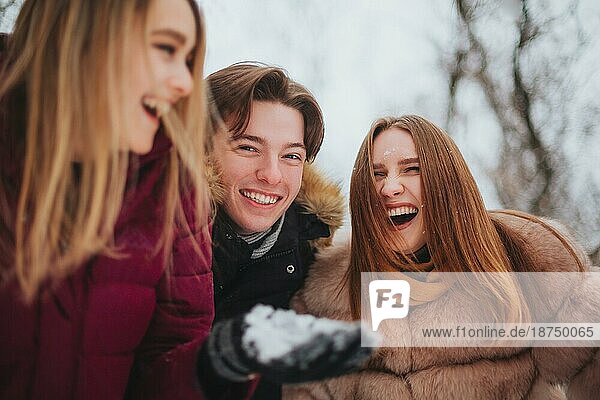 Gruppe von vier fröhlichen besten Freunden  die das kalte Wetter und den ersten Schnee genießen  während sie im Freien über schneebedeckten Bäumen stehen  die Hände hochheben und versuchen  fallende Schneeflocken aufzufangen  und mit einem glücklichen Lächeln nach oben schauen