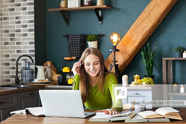 Junge  glückliche Freiberuflerin sitzt zu Hause am Tisch mit Laptop  macht sich Notizen  starrt nachdenklich in die Luft  denkt über neue Ideen nach  Bloggerin auf der Suche nach Inspiration. Freiberufliches Konzept