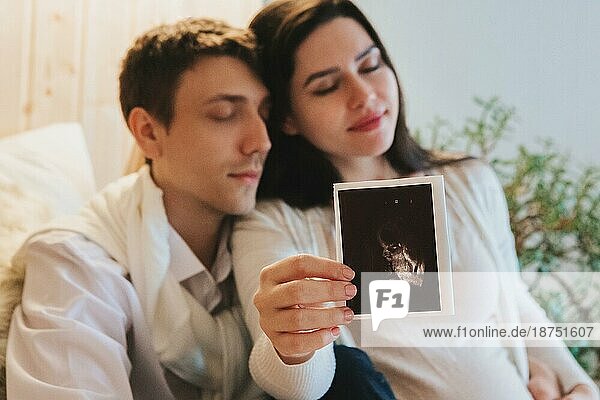 Junge glückliche schwangere Frau hält Schwangerschaft Ultraschall  zeigt Sonogramm Bild zu angenehm überrascht Mann weinen vor Glück. Familienpaar wartet auf das Baby. Selektiver Fokus