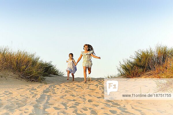 Zwei glückliche fröhliche kleine Schwestern laufen Hand in Hand auf Sand auf sonnigen Abend Strand  lustige Mädchen lachend und lächelnd verbringen Zeit mit der Familie am Meer. Reisen und Sommerurlaub Konzept