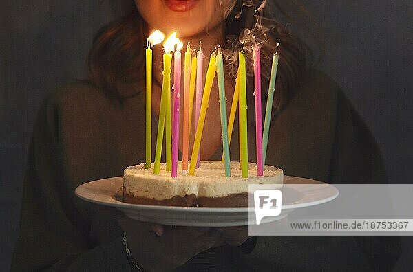 Junge lächelnde Frau hält selbstgebackenen Geburtstagskuchen mit brennenden Kerzen  während sie drinnen steht  Seitenansicht. Weibliche bringen Bday Kuchen. Geburtstag Traditionen und Feier Konzept