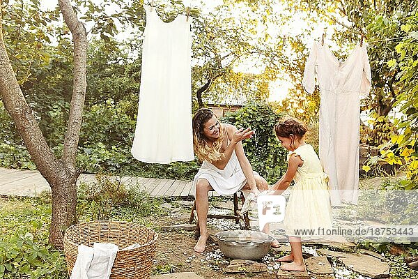 Charmantes kleines Mädchen  das seiner Mutter mit einem Weidenkorb hilft  während es die Wäsche im Garten im Sommer aufhängt