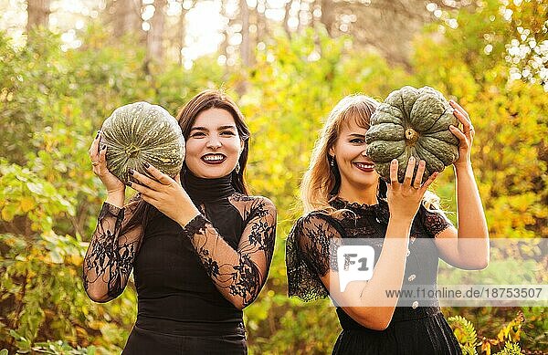 Zwei Freundinnen  die gruselige grüne Kürbisse vor ihrem Gesicht halten  stehen isoliert über Herbstwald Hintergrund. Herbstferien  halloween Dekorationen und Menschen Konzept