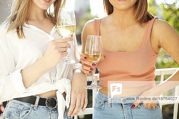 Zwei stilvolle glückliche Frauen versammeln sich im Sommer zu einer Party und genießen die gemeinsame Zeit beim Trinken von Weißwein Nahaufnahme