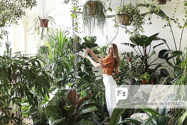 Junge Frau mit Zöpfen lächelt und kümmert sich um Topfpflanzen bei der Gartenarbeit am Wochenende zu Hause