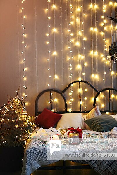 Tablett mit Dekorationen und Geschenkbox auf bequemen Bett in gemütlichen Schlafzimmer für Weihnachtsfeier in der Nacht dekoriert platziert